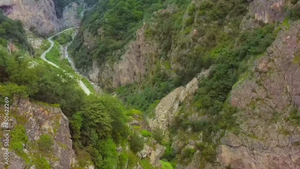 Aerial view of a mountain gorge with a road and a couple of cars. Flight straight along the bottomless gorge view of rocks with rare vegetation, a mountain road and a couple of cars Aerial view of a mountain gorge with a road and a couple of cars. Flight straight along the bottomless gorge view of rocks with rare vegetation, a mountain road and a couple of cars