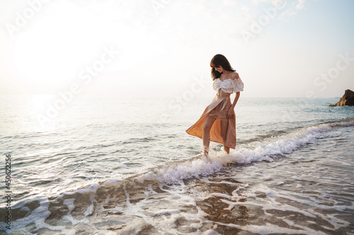 Lonely young woman walks on the seashore at sunset