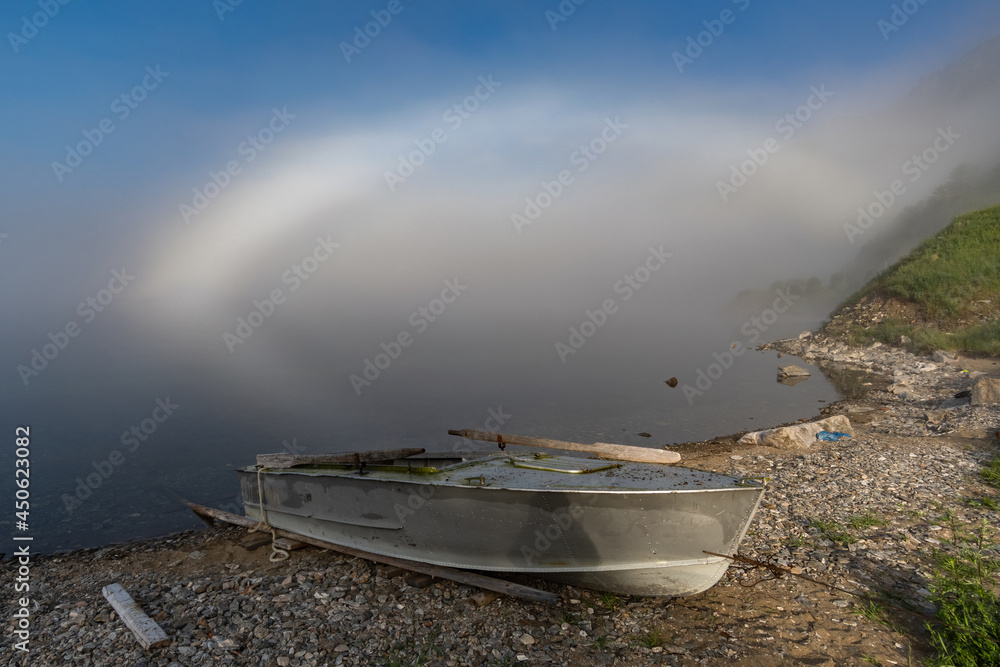 A boat on the shore of Lake Baikal and a white rainbow in the fog