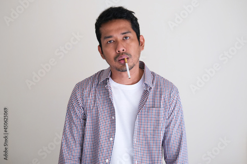 Adult Asian man smoking with very messy face expression photo
