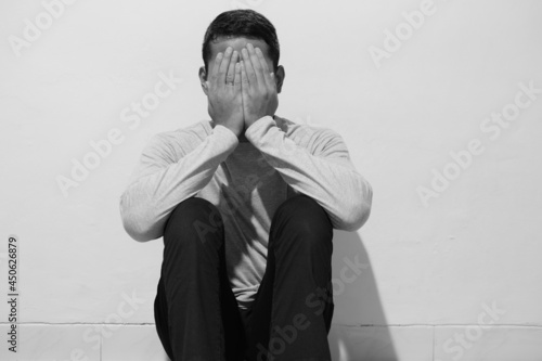 Black and white photo of adult man closing his face with hand showing sadness photo
