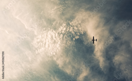 Silhouetted airplane flying high in the sky between the clouds 