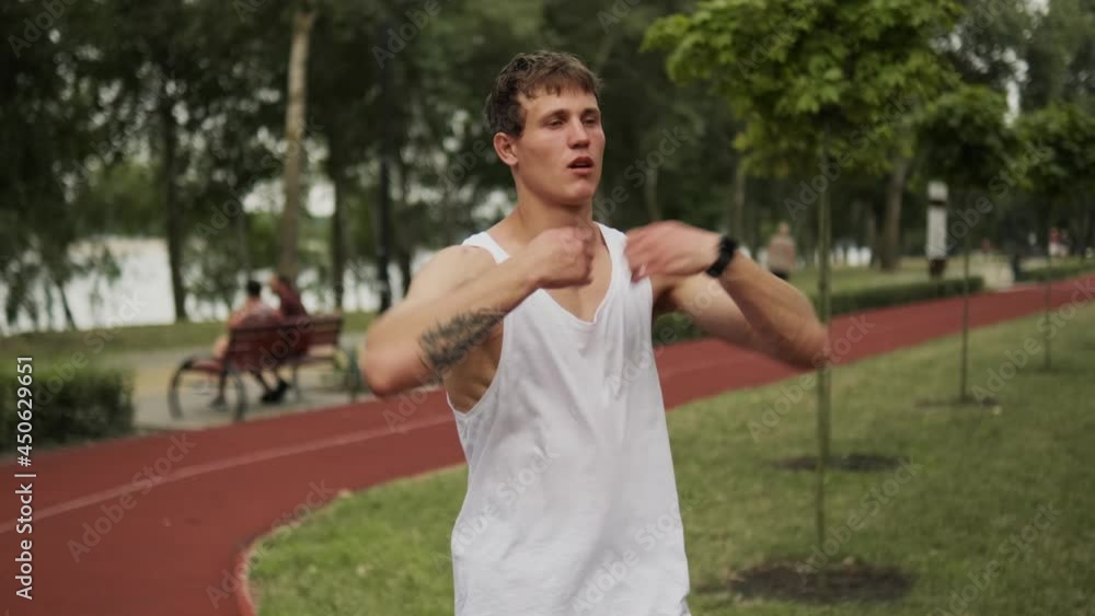 A muscular guy is stretching his arms while walking outdoors A muscular guy is stretching his arms while walking outdoors