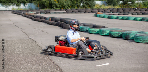 A girl or a woman in a hard hat rides a go-kart on a special track fenced with rubber wheels. Active recreation and sports on transport. Preparation and training for competitions. 
