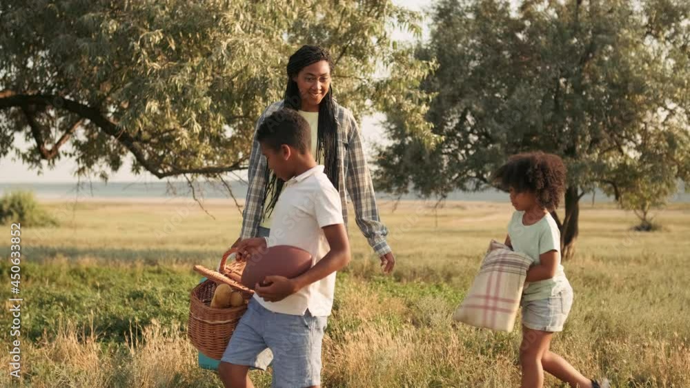 A pleased family is going to have a picnic time while carrying things walking the meadow A pleased family is going to have a picnic time while carrying things walking the meadow