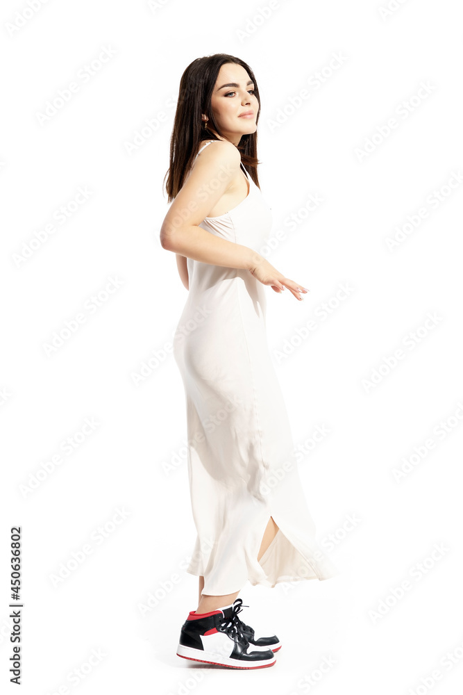 Side view of carefree young woman in white dress and sneakers dancing. Full body portrait isolated on white background Side view of carefree young woman in white dress and sneakers dancing. Full body portrait isolated on white background