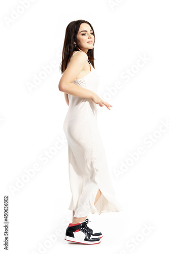 Side view of carefree young woman in white dress and sneakers dancing. Full body portrait isolated on white background © sharplaninac