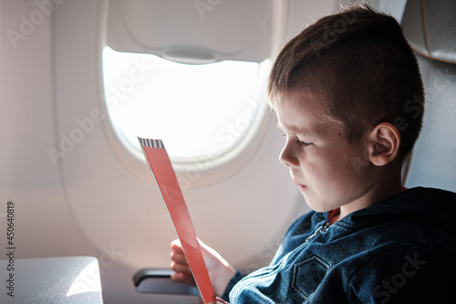 Cute little boy traveling by an airplane. Six years old boy reads the brochure.