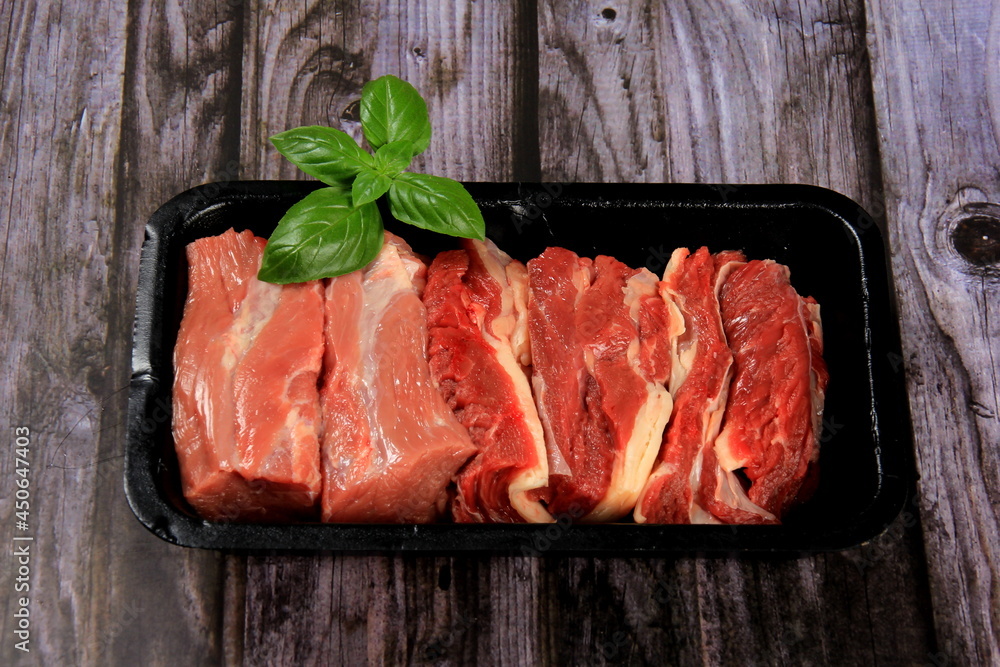 Raw beef meat in a black plastic container. Opened black plastic tray with raw cut meat