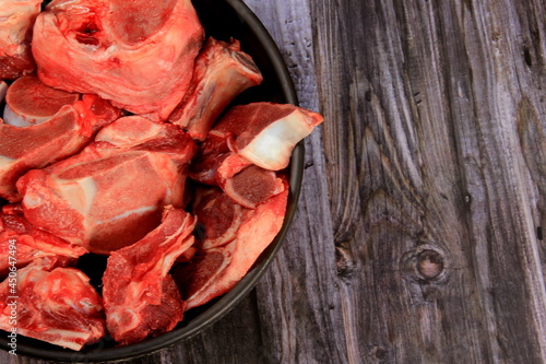 Raw beef bones in round clay bowl on wooden table. Beef selection for soup, Copy space 