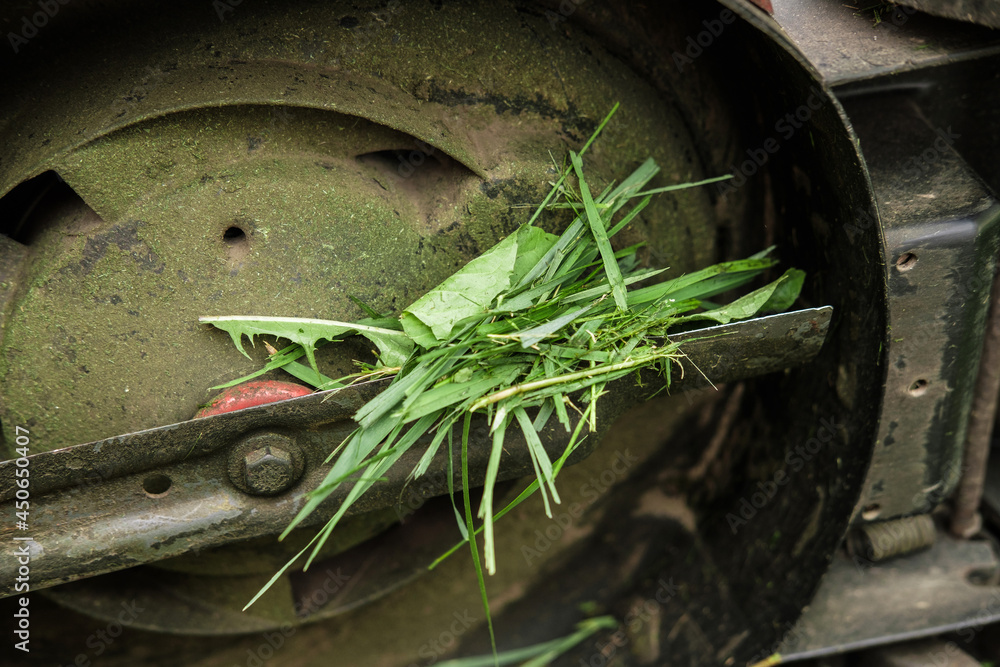 Broken lawn mower on lush green grass. The lawn mower is jammed with grass. Broken lawn mower on lush green grass. The lawn mower is jammed with grass.