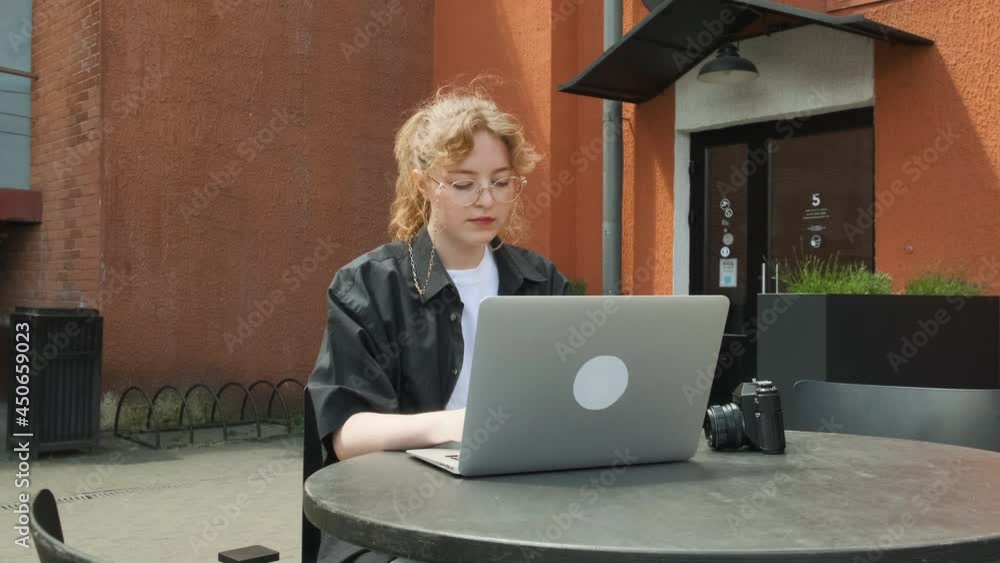 A young girl works remotely in a cafe on a summer terrace. A freelancer works outdoors. High quality 4k footage A young girl works remotely in a cafe on a summer terrace. A freelancer works outdoors. High quality 4k footage
