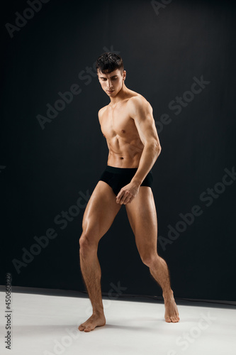 sexy man with naked muscular body in black panties dark background