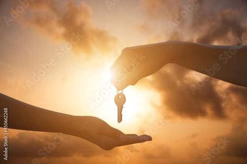 Silhouette of hand holding keys over the hand on overcast sky and sunrise background. It is the key to success.