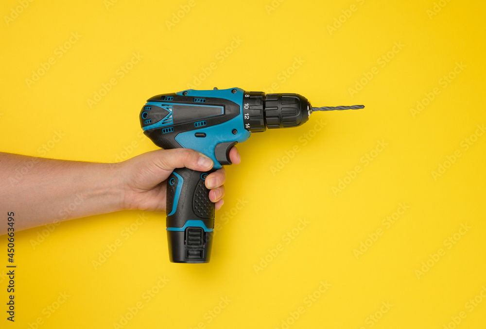 female hand holds a cordless drill on a yellow background. Tool for work female hand holds a cordless drill on a yellow background. Tool for work