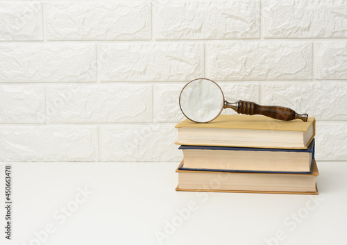 a wooden magnifying glass lies on a stack of books, new knowledge and discoveries are reading books