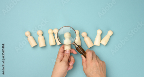 wooden men and a magnifying glass on a blue background. Recruitment concept, search for talented and capable employees, career growth photo