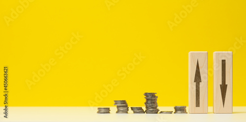stacks of metal money and two wooden bars with arrows on a white table  yellow background. The concept of depreciation and depreciation of the exchange rate  the fall of the economy