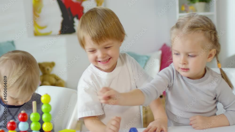 Excited little boys and girl making toy block tower come crashing down and smiling while playing together in kindergarten Excited little boys and girl making toy block tower come crashing down and smiling while playing together in kindergarten