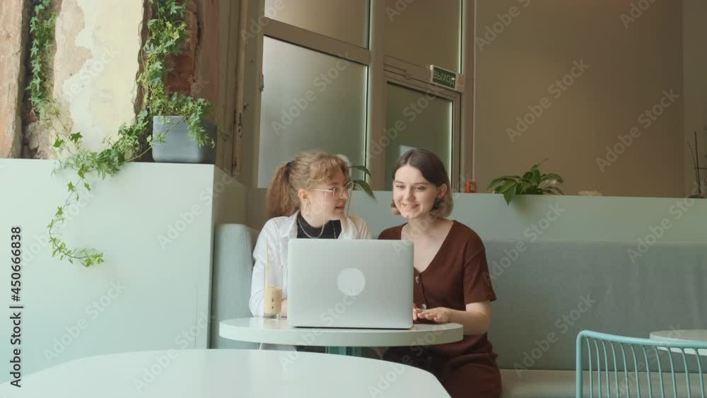 Young girls work remotely in a cafe on the summer terrace. Freelancers communicate with colleagues via video link. High quality 4k footage Young girls work remotely in a cafe on the summer terrace. Freelancers communicate with colleagues via video link. High quality 4k footage