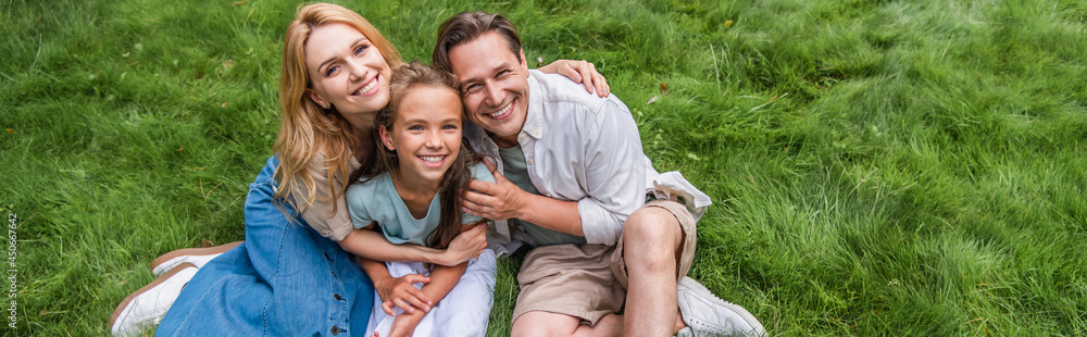 High angle view of parents hugging smiling kid on grass, banner High angle view of parents hugging smiling kid on grass, banner