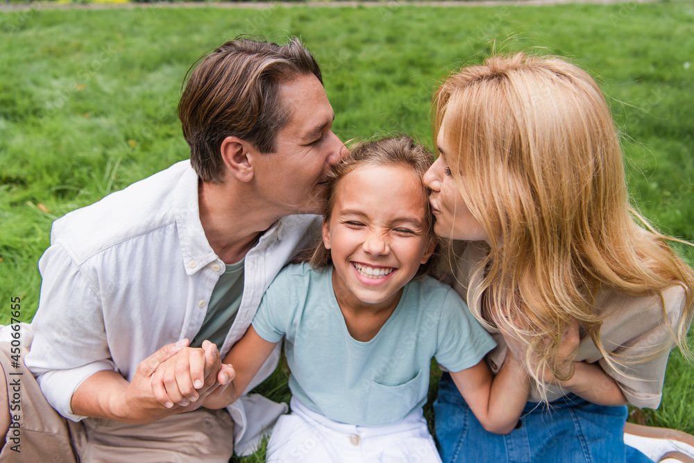 Parents kissing daughter on lawn