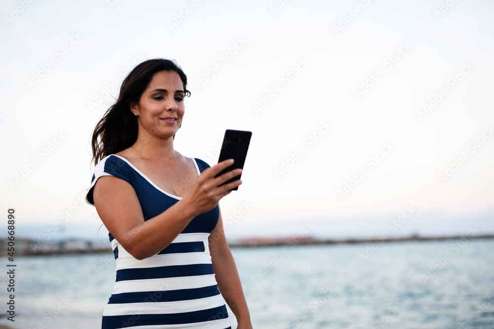 Beautiful young woman using the phone at the beach. Smiling happy woman typing a message while resting at the beach.