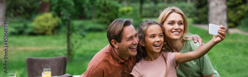 Smiling girl talking selfie with parents outdoors, banner