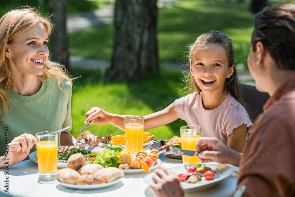 Positive family looking at father on blurred foreground during picnic outdoors