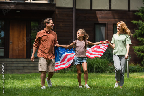 Kid with american flag holding hands of parents on lawn