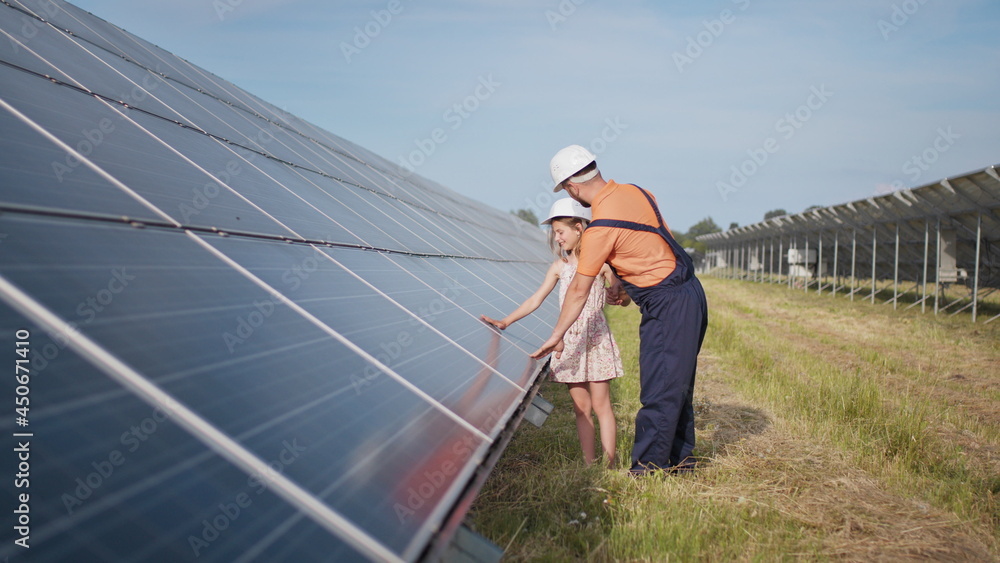 A father working in a solar power plant tells his daughter about his work, shows green energy, solar panels. Shooting at a solar power plant. The child studies solar energy