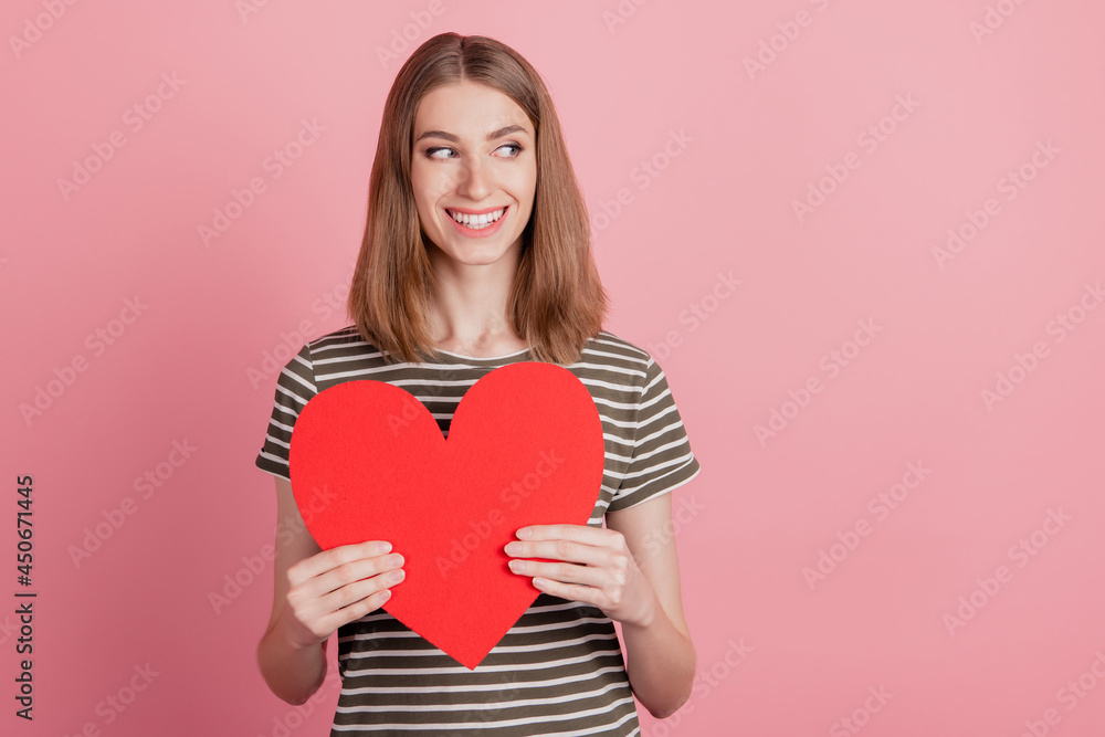 Portrait of nice cute attractive cheerful lady wearing striped t-shirt holding in hands large paper heart isolated over pink background Portrait of nice cute attractive cheerful lady wearing striped t-shirt holding in hands large paper heart isolated over pink background