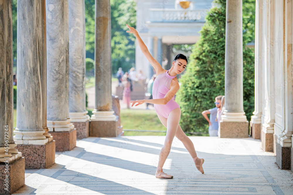 Slender ballerina in pointe shoes and wearing silhouette costume dancing against the background of antique architecture in park Slender ballerina in pointe shoes and wearing silhouette costume dancing against the background of antique architecture in park