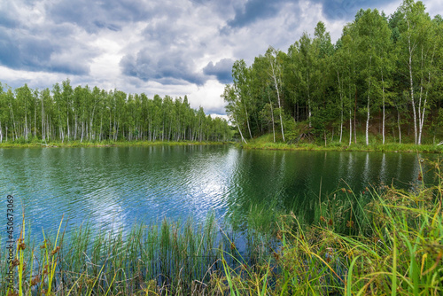 Forest on the shore of the lake. Reflection of the sky and forest in the water.
