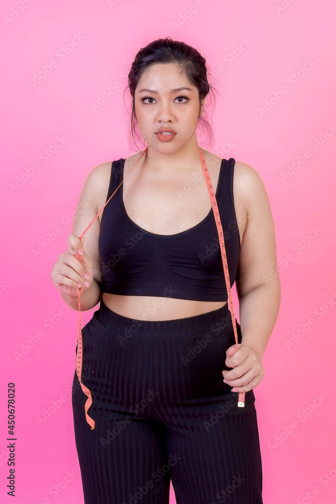 Portrait beautiful Asian fat women , Fat girl ,Chubby, overweight plus size in sports wear with measure tape on her neck isolated on pink background - lifestyle Woman diet weight loss overweight