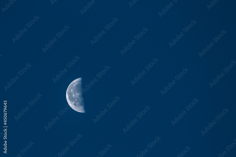 Half a moon in the daytime blue sky. Craters and lunar seas Half a moon in the daytime blue sky. Craters and lunar seas