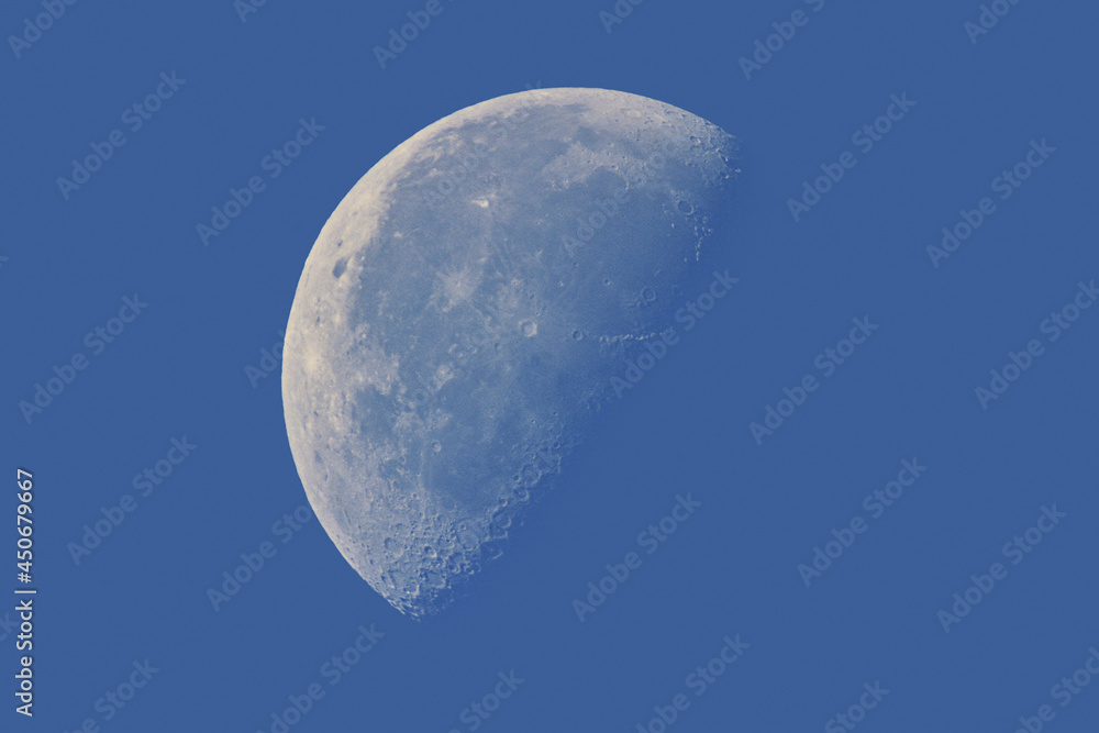 Half a moon in the daytime blue sky. Craters and lunar seas Half a moon in the daytime blue sky. Craters and lunar seas