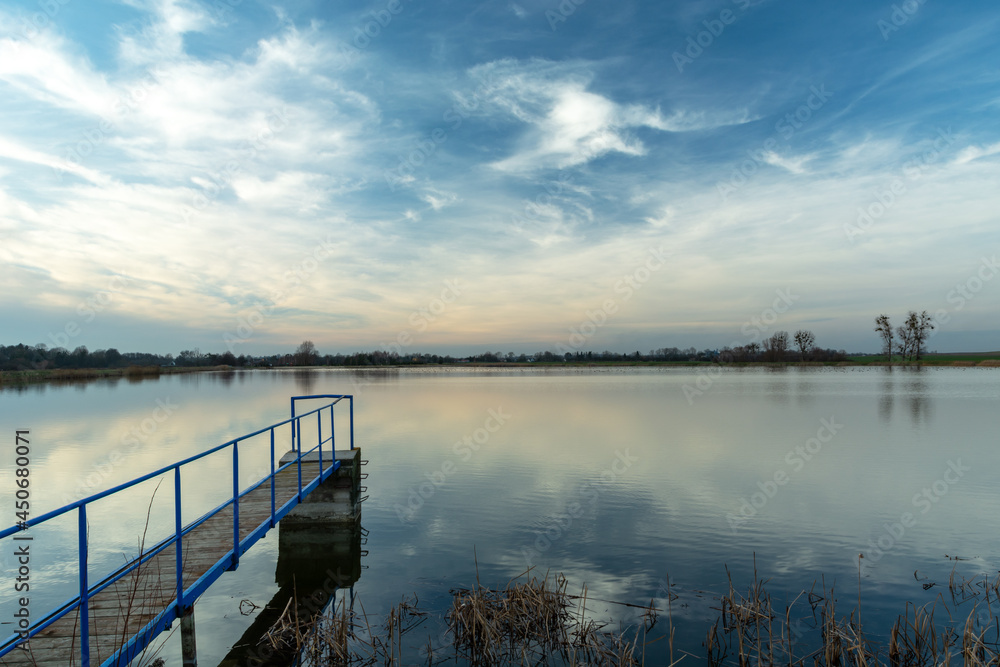 Fototapeta premium A narrow jetty on a calm lake and clouds