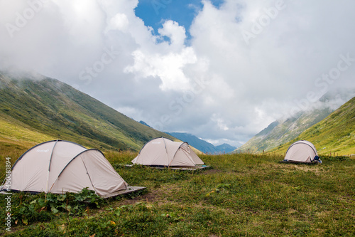 Green mountain Valley in the mountains of Sochi  Russia. Three gray tourist tents. Picturesque view  wild flowers. Clouds and blue sky. Krasnaya Polyana.