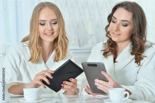 Two beautiful young women in bathrobes using digital devices