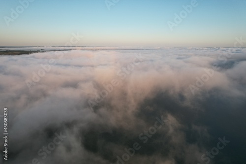 Aerial view of large river with fog above the water. Colorful landscape with forest in low clouds, river, meadow in fog, orange sky with sun in the morning. .Top view. Nature