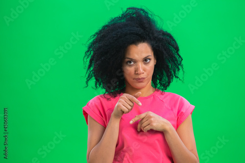 Portrait of young female African American upset and resentful looking to the side. Black woman with curly hair in pink tshirt poses on green screen in the studio. Close up. photo