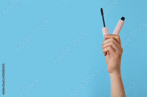 Woman holding mascara on light blue background, closeup. Space for text