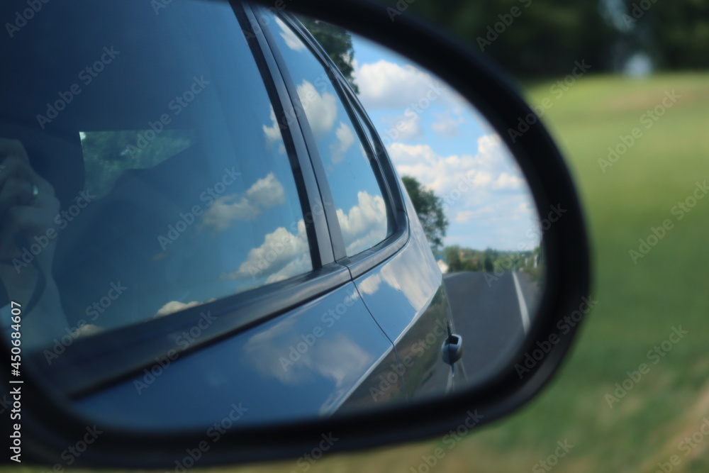 Road and blue sky with clouds. Rear view in car mirror. Road travel concept.