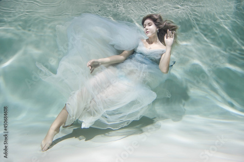 Girl underwater. model in water in a beautiful dress swims like a fish.In a blue flying dress. 