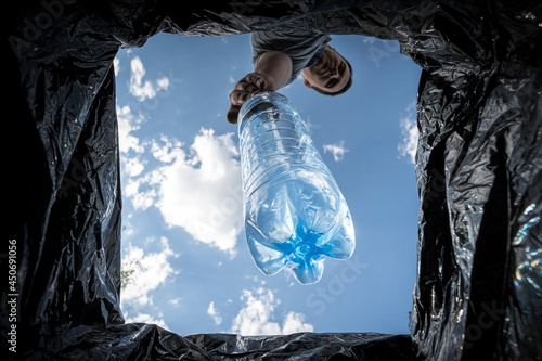 man throws empty plastic bottle into a trash can. Bottom view from the trash can. The problem of recycling and pollution of the planet with garbage.