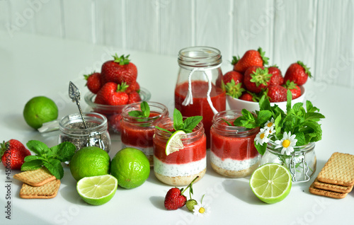 Homemade cheesecake with strawberry and cottage cheese cream in a glass jar.fresh green lime, mint and chia on white background.summer dessert without baking