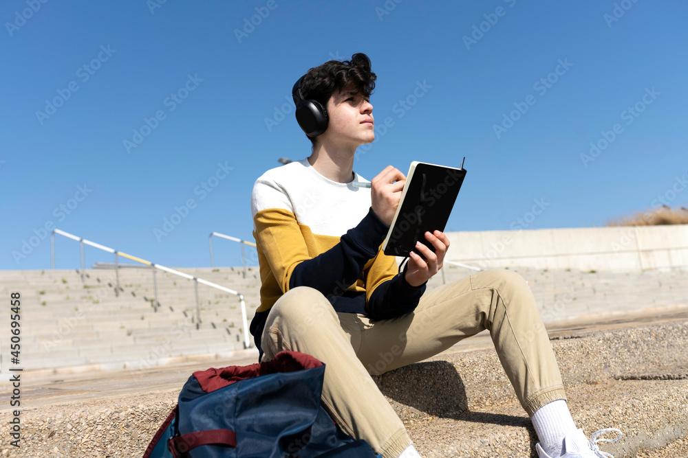 © Cavan Images - Young male writing notes in a notebook sitting on a staircase