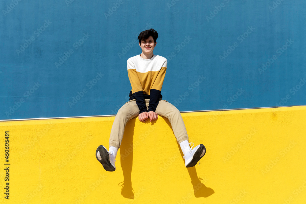 Confident man looking to camera while sitting on yellow retaining wall Confident man looking to camera while sitting on yellow retaining wall