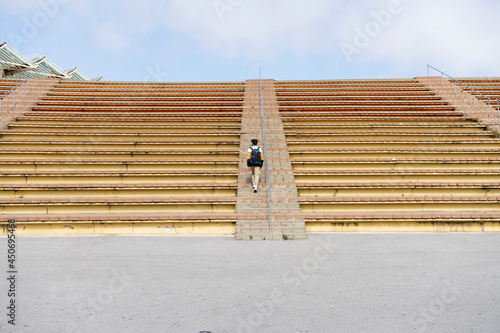 Rear view of a young student with backpack going up stairs of bleacher